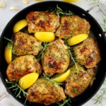 Greek Lemon Chicken in skillet with lemon wedges and fresh rosemary