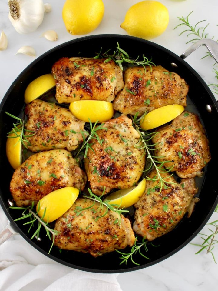 Greek Lemon Chicken in skillet with lemon wedges and fresh rosemary