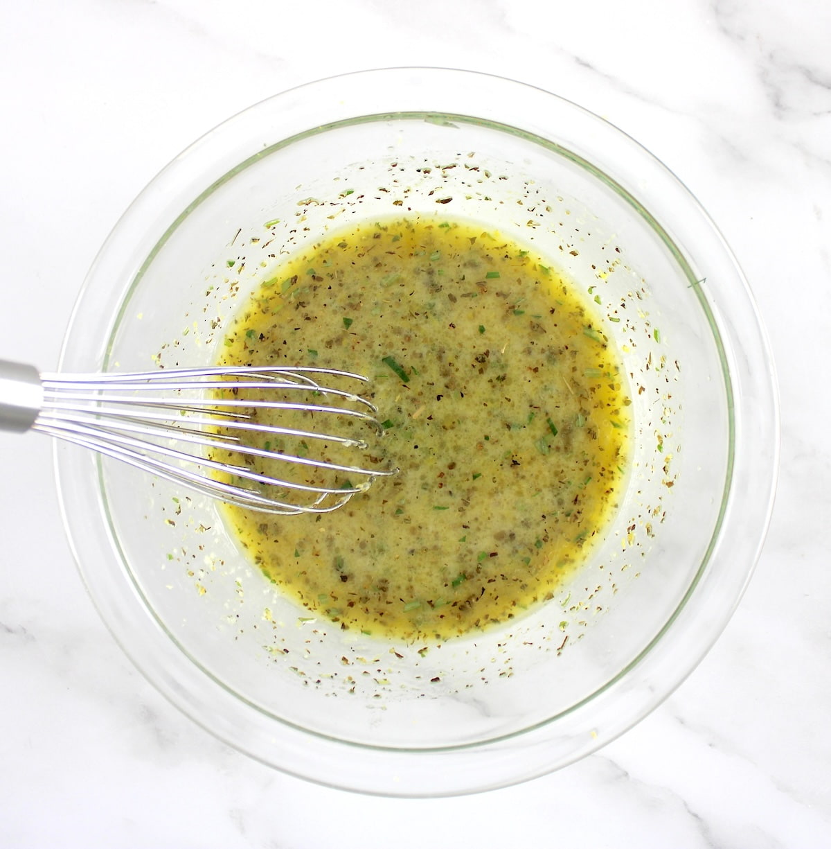 Greek Lemon Chicken marinade in glass bowl with whisk