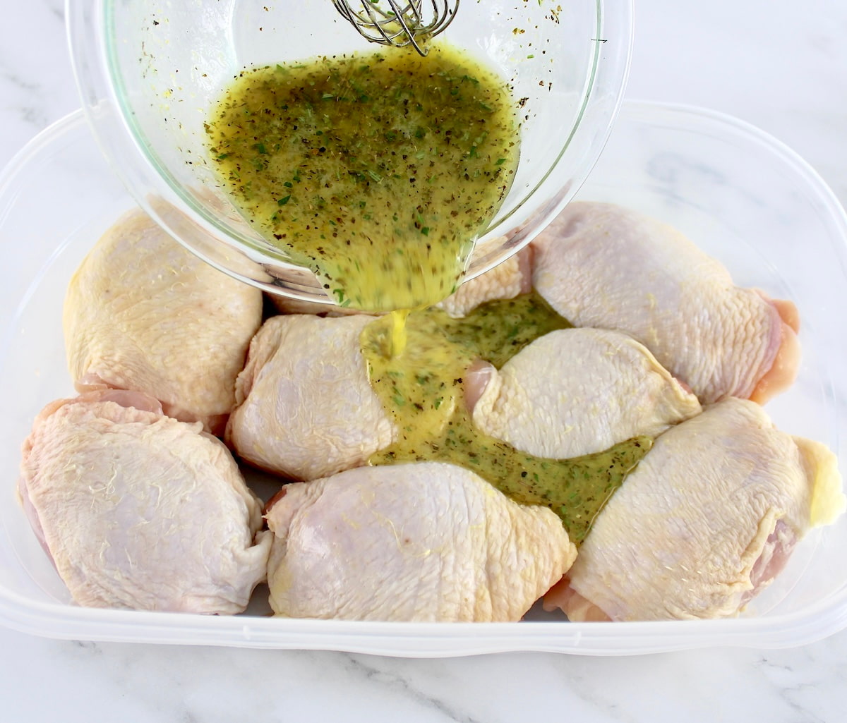 Greek Lemon Chicken marinade being poured over 8 raw chicken thighs 