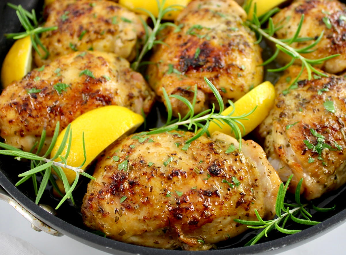 closeup of Greek Lemon Chicken in skillet with rosemary and lemon wedges