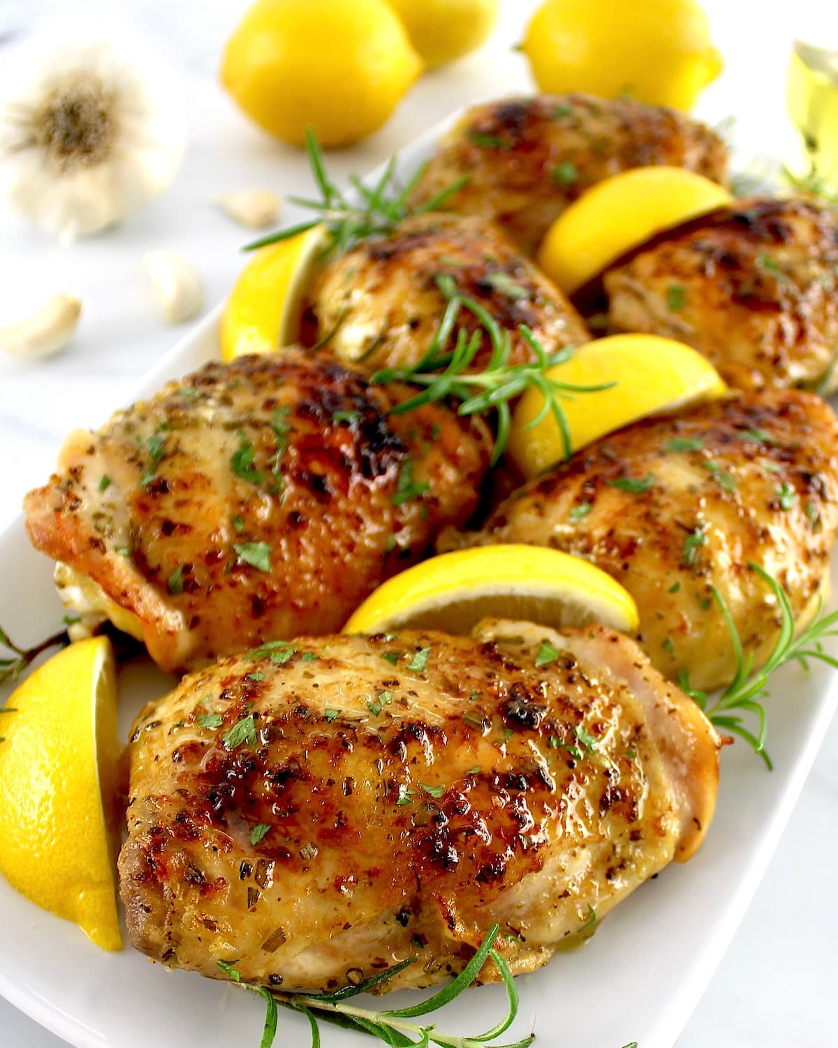 Greek Lemon Chicken on white plate with lemon wedges and rosemary