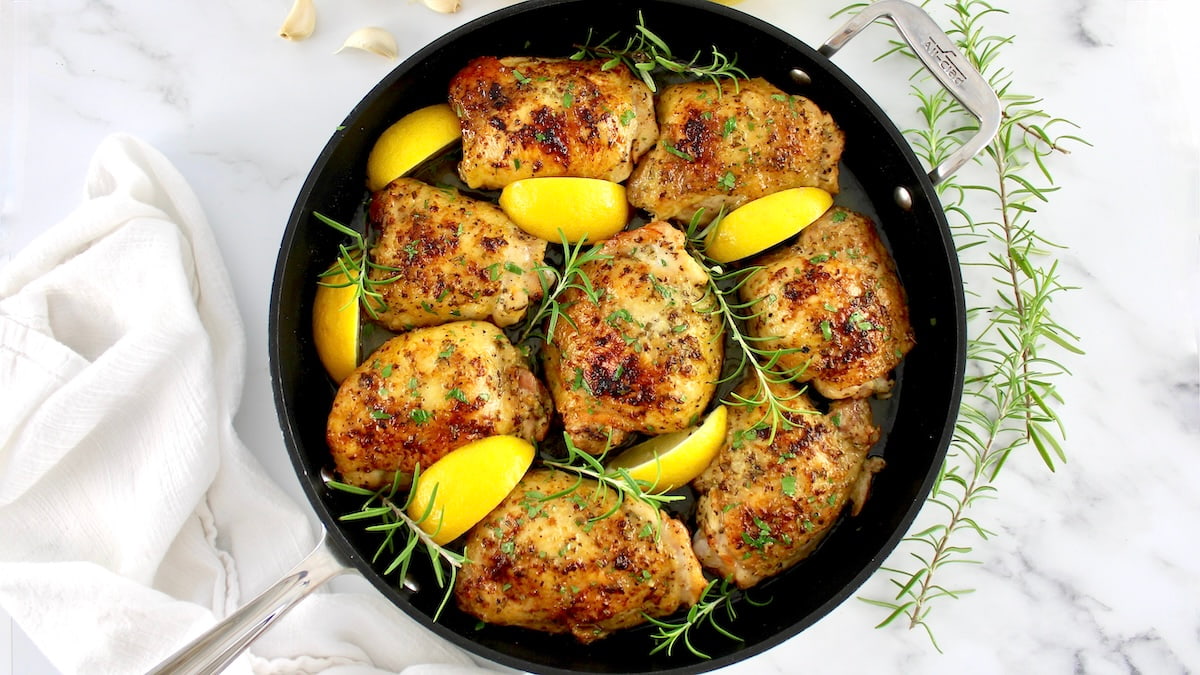 overhead view of Greek Lemon Chicken in skillet with lemon wedges and rosemary