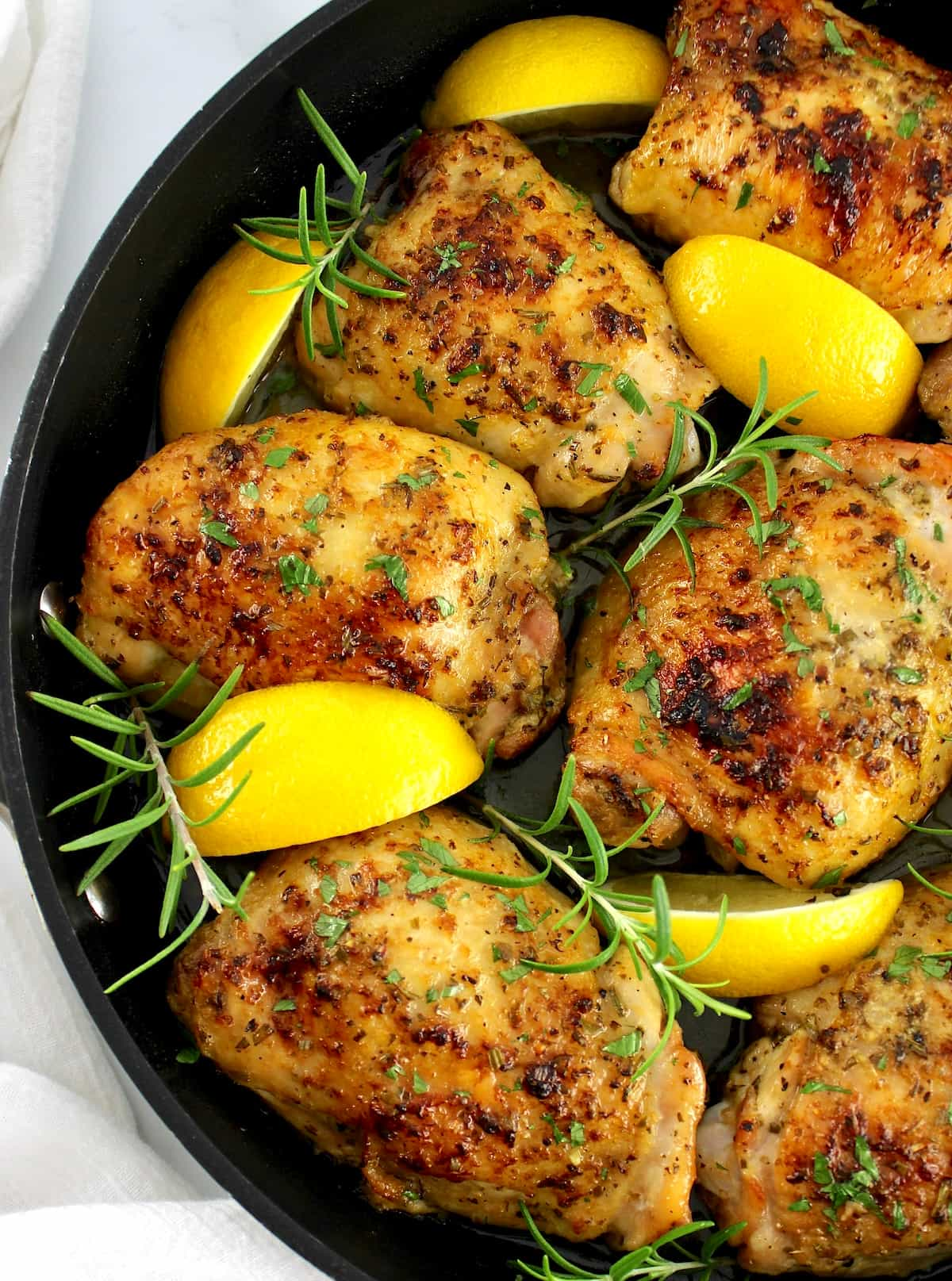 closeup of Greek Lemon Chicken in skillet with lemon wedges and sprigs of rosemary