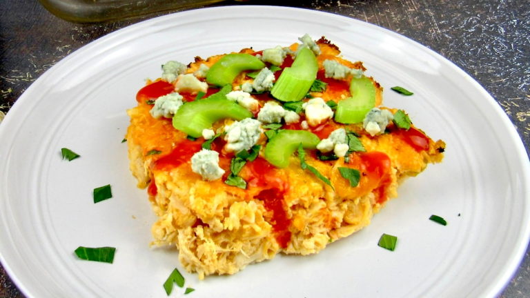 Keto Buffalo Chicken Casserole slice on white plate with chopped celery and buffalo sauce on top