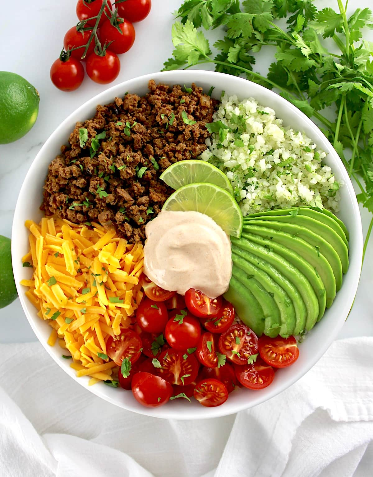 overhead view of Keto Burrito Bowl in white bowl with veggies in back