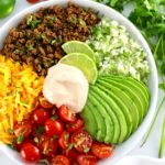 overhead view of Keto Burrito Bowl in white bowl with cilantro and tomatoes in back