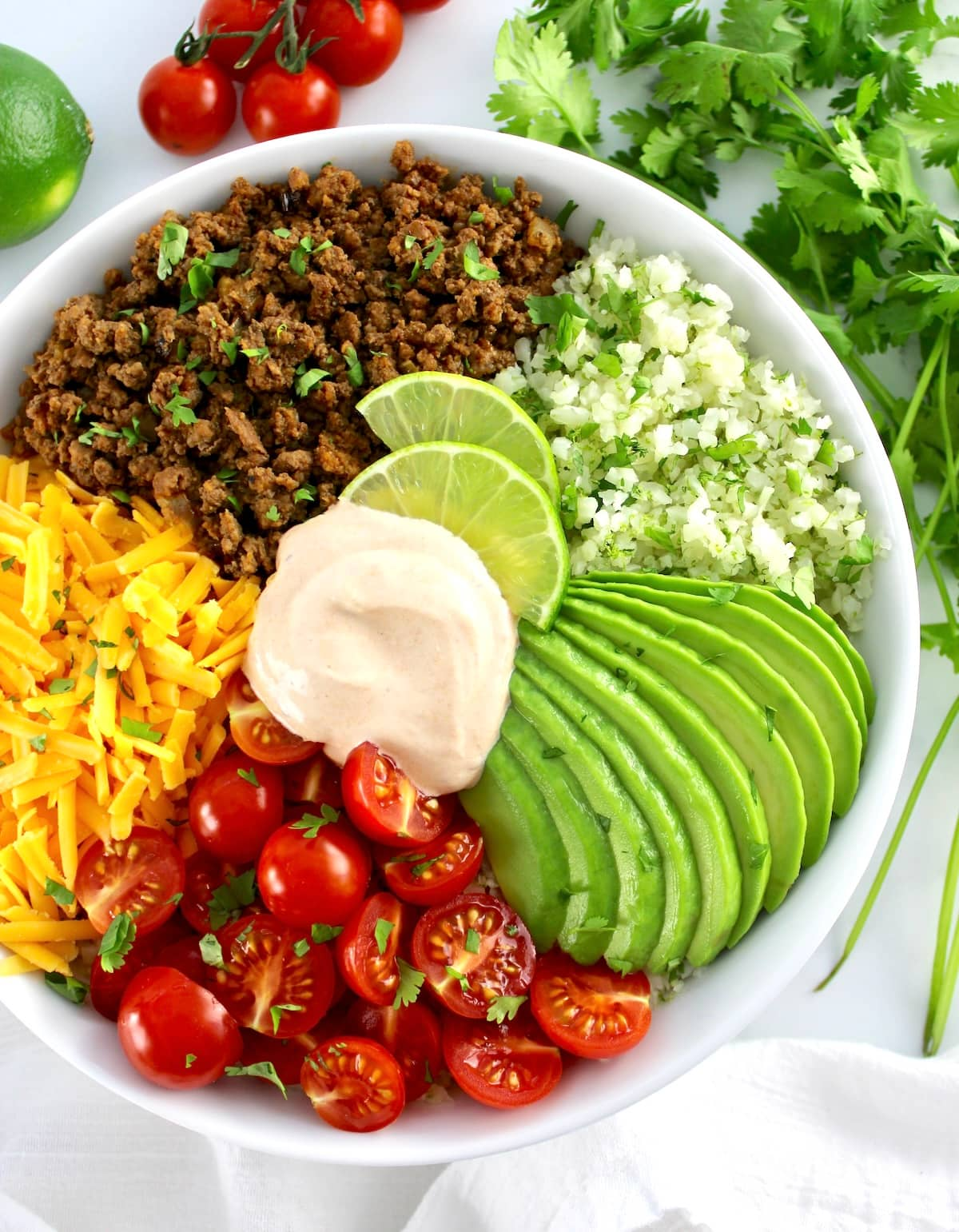 overhead view of Keto Burrito Bowl in white bowl with cilantro and tomatoes in back