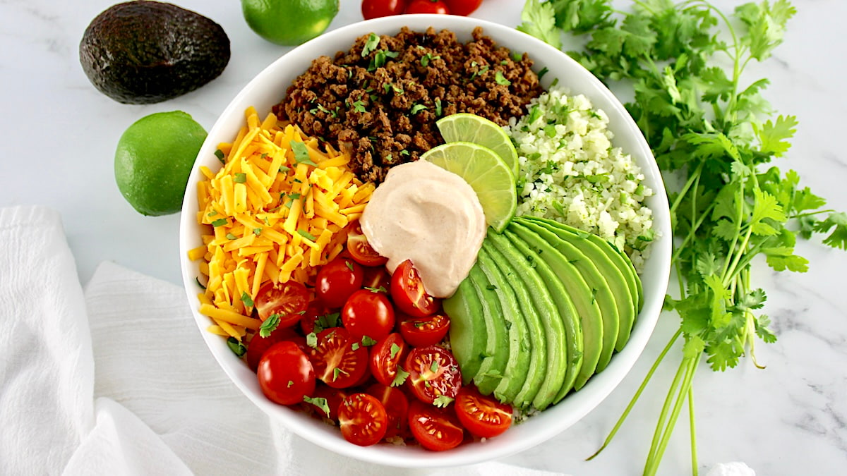 overhead view of Keto Burrito Bowl in white bowl with cilantro and tomatoes in back