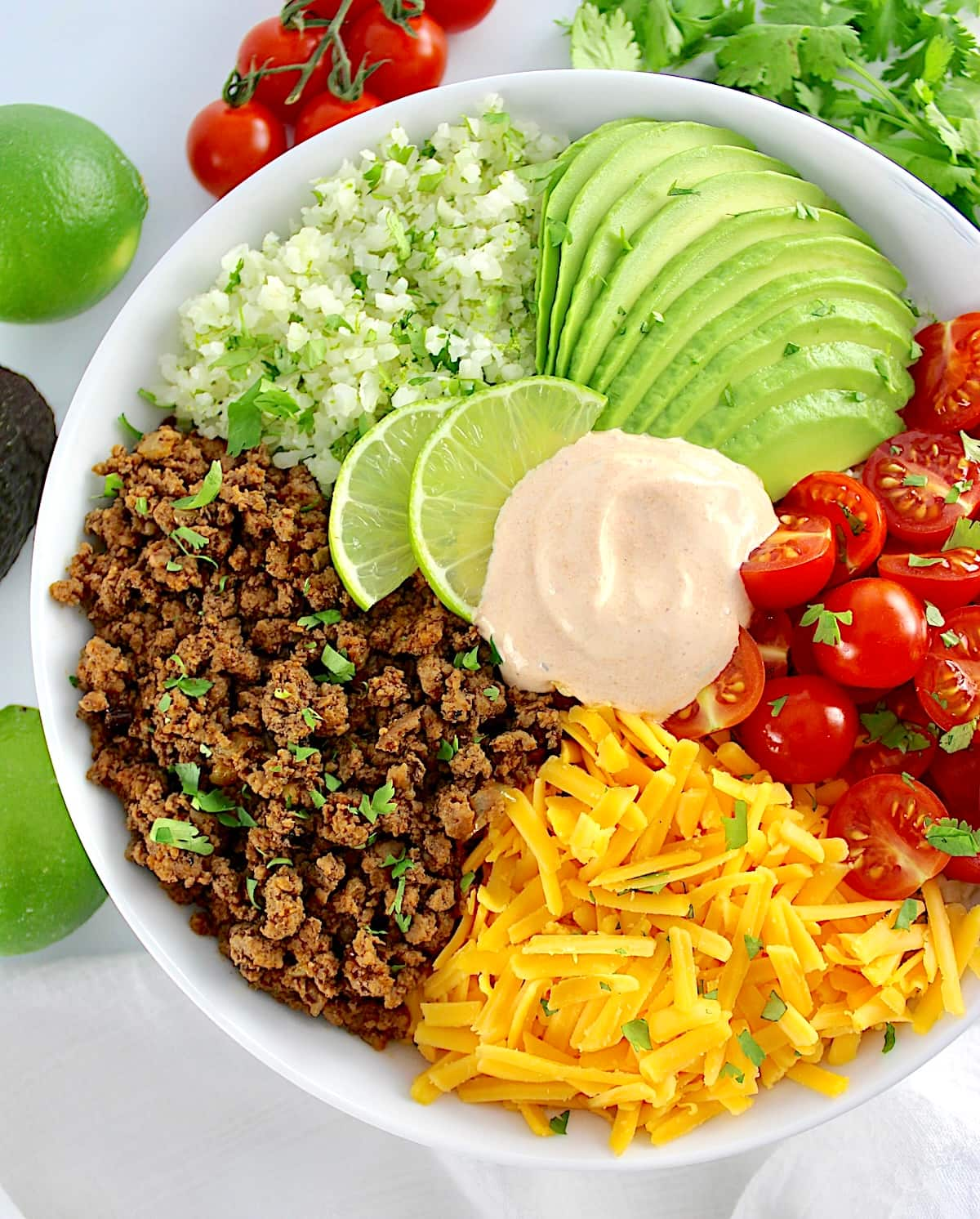 closeup of Keto Burrito Bowl in white bowl with tomatoes and lime in back