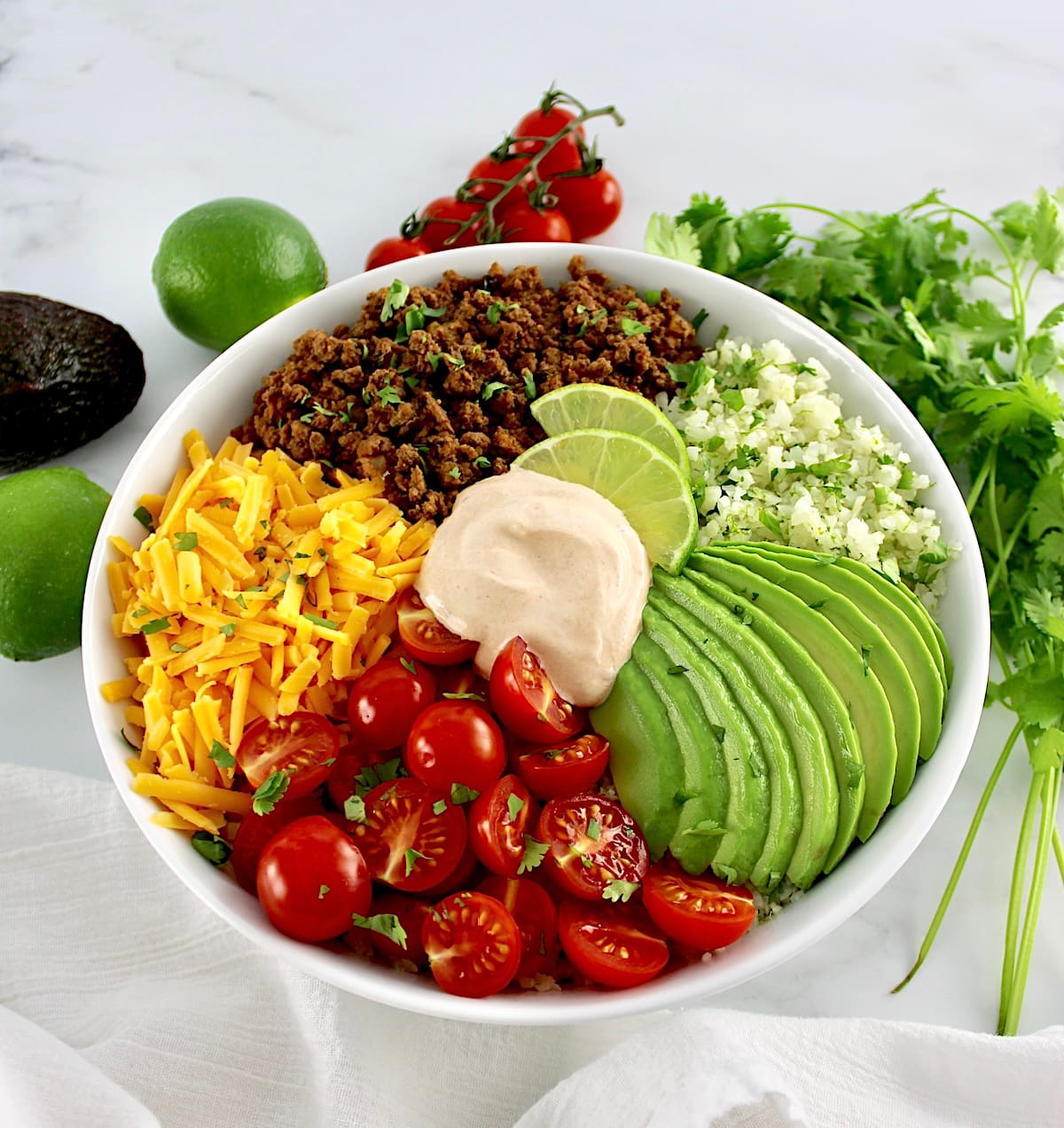 overhead view of Keto Burrito Bowl in white bowl with veggies in back