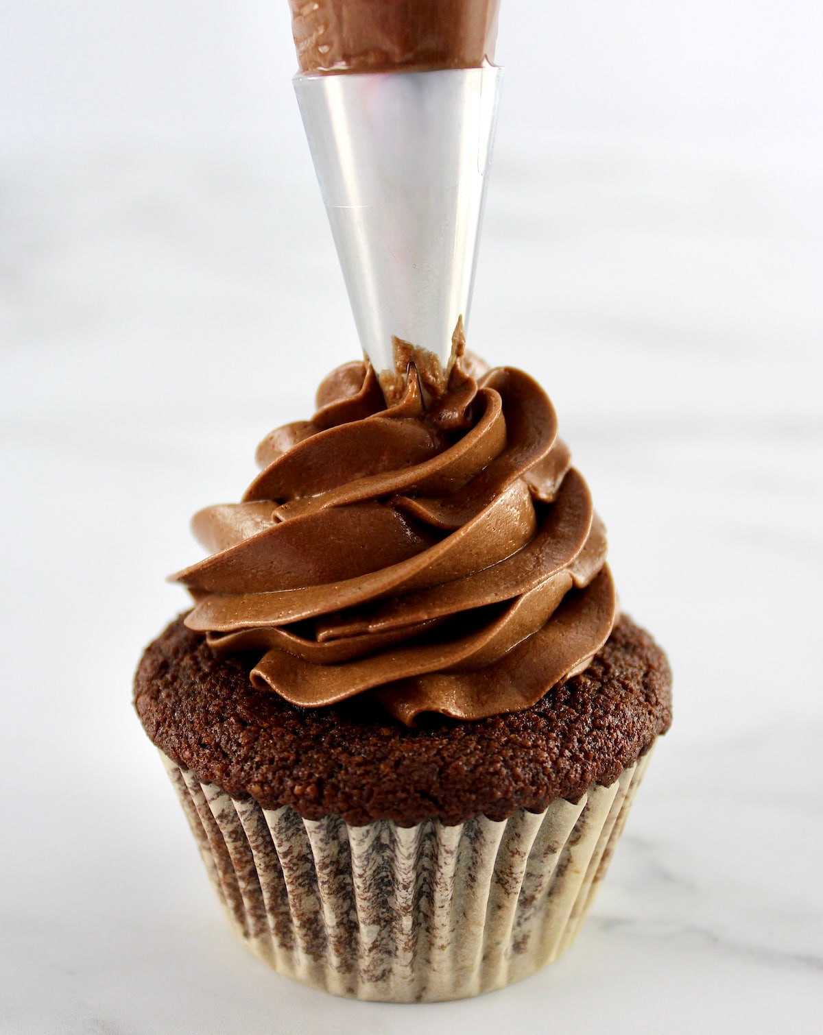 Keto Chocolate Frosting being piped onto a chocolate cupcake