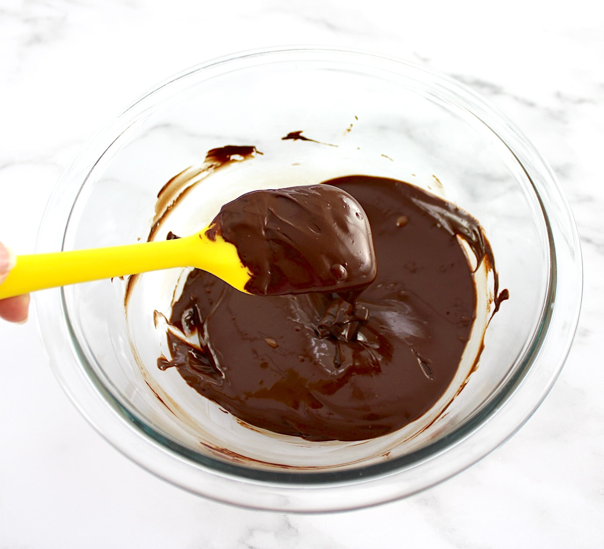 melted sugar-free chocolate in glass bowl with yellow spoon holding up some