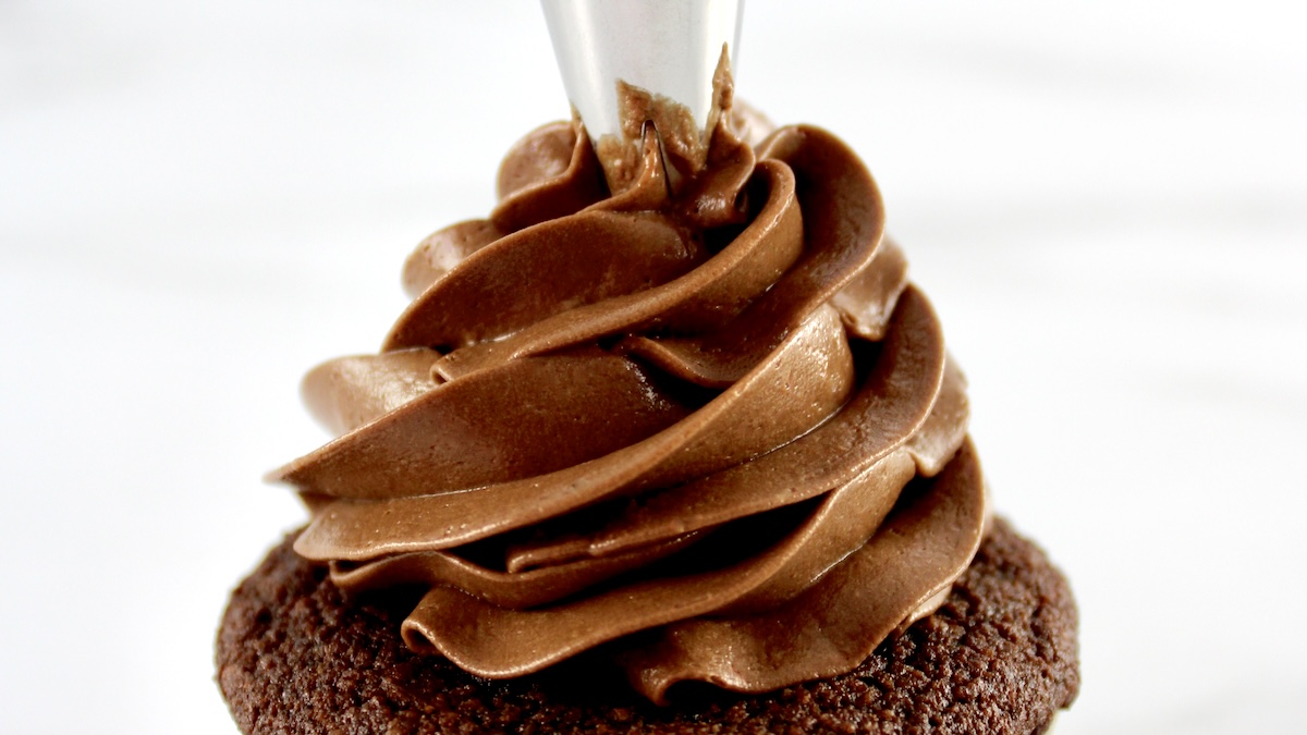 closeup of Keto Chocolate Frosting being piped onto chocolate cupcake