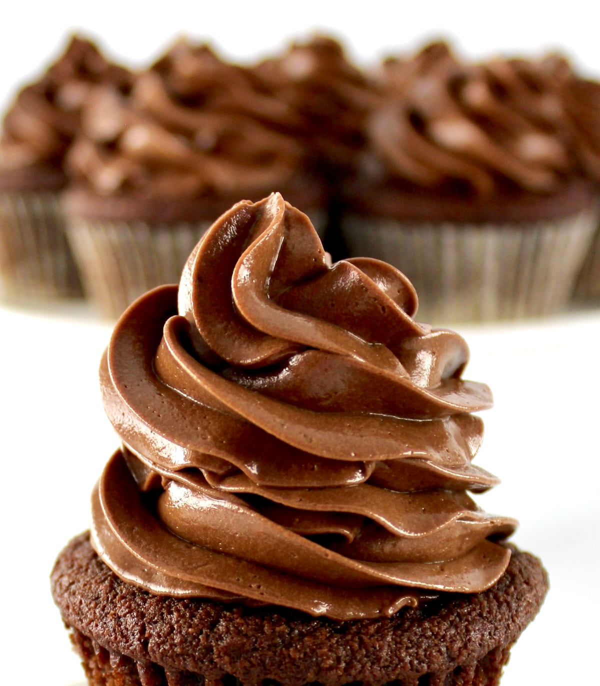 closeup of Keto Chocolate Frosting on chocolate cupcake with more cupcakes in back