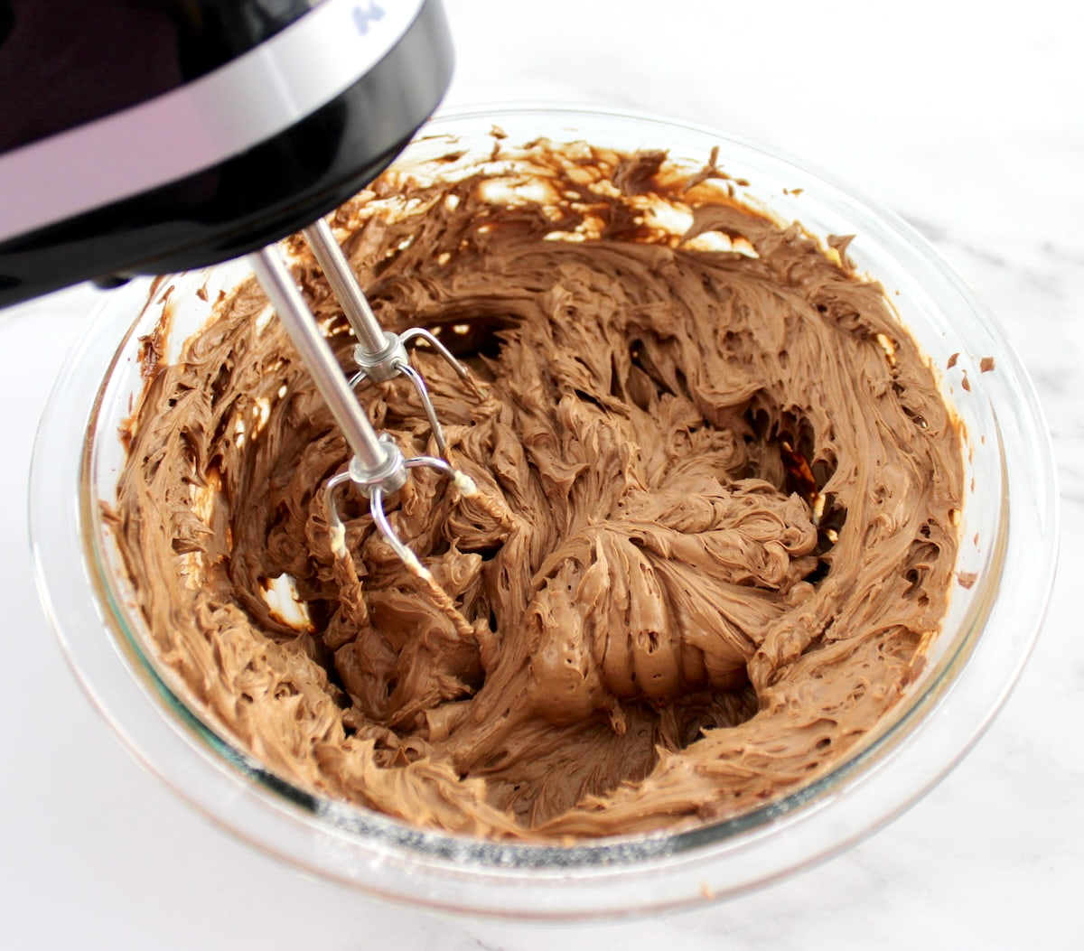 Keto Chocolate Frosting being mixed with hand mixer in glass bowl