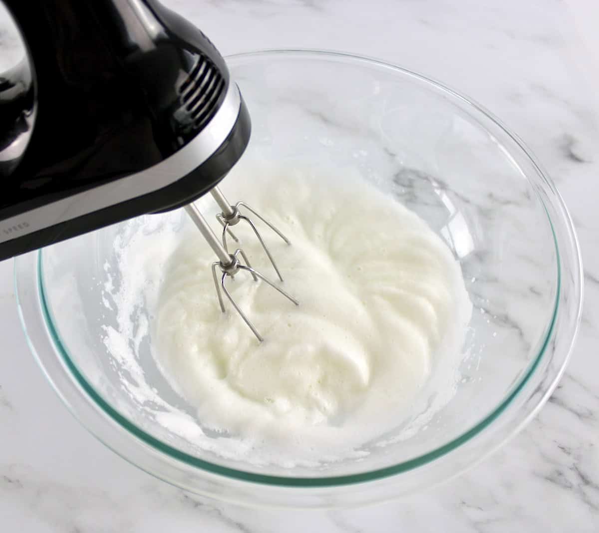 egg whites being whipped with hand mixer in glass bowl