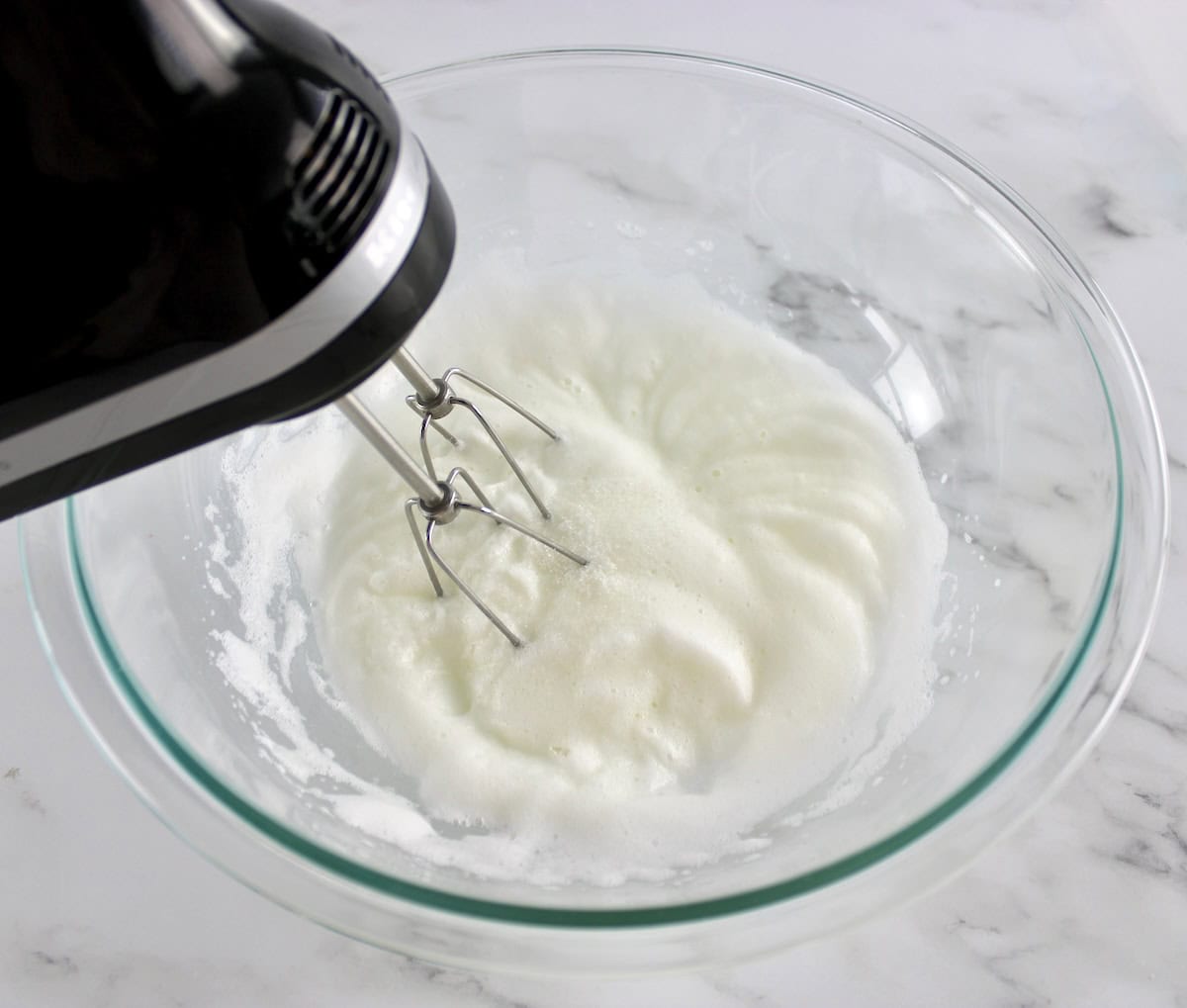 egg whites and sweetener being whipped up in glass bowl with hand mixer