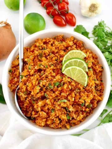 Mexican Cauliflower Rice in white bowl with spoon and 3 lime slices on top