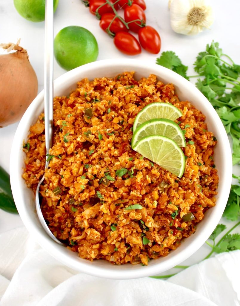 Mexican Cauliflower Rice in white bowl with spoon and 3 lime slices on top