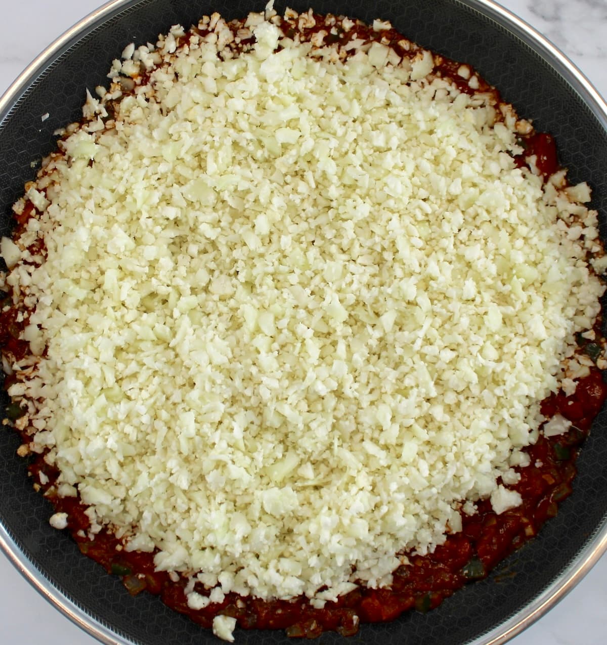 cauliflower rice in skillet with tomato sauce under