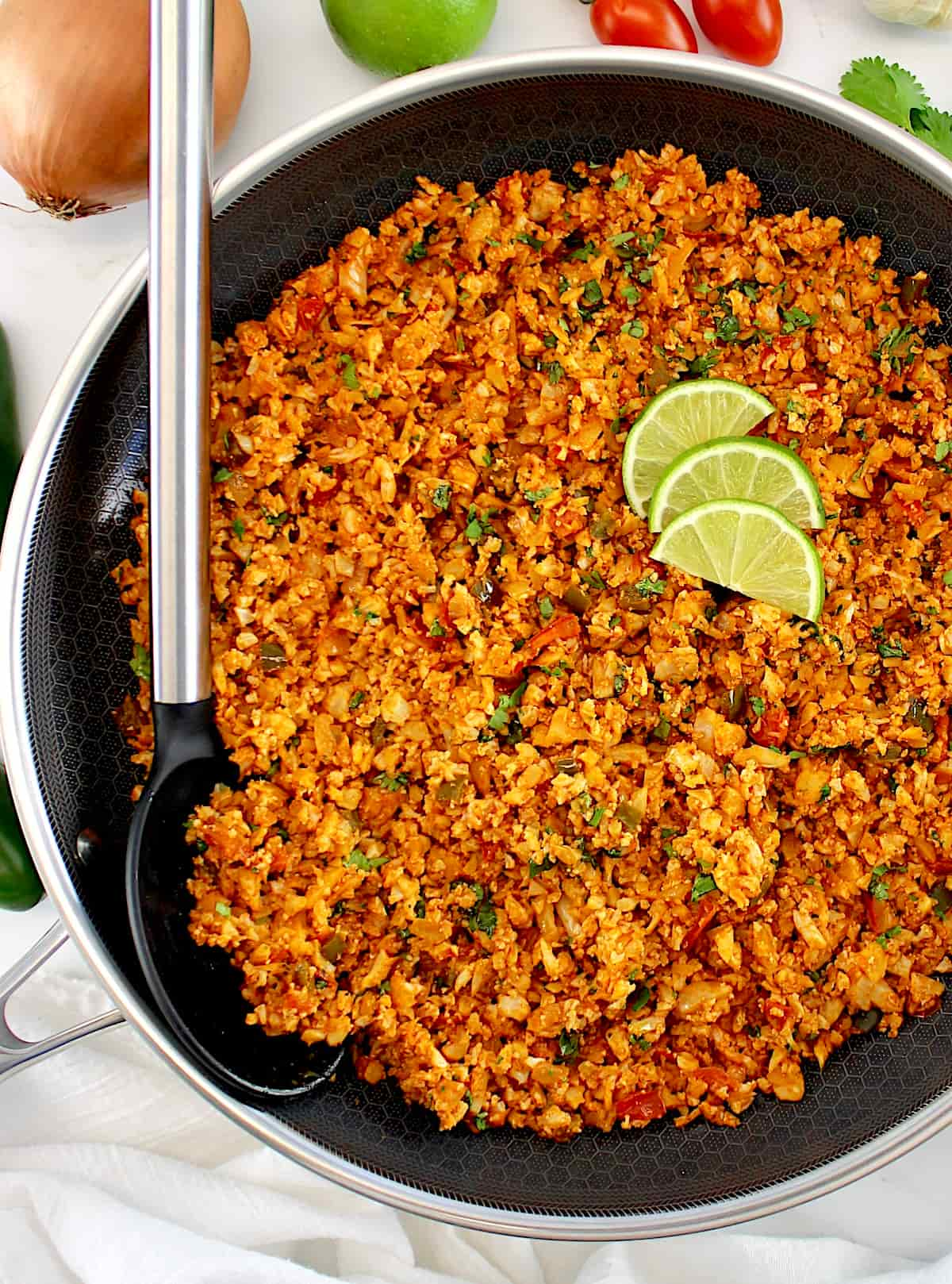 Mexican Cauliflower Rice in skillet with 3 lime slices and serving spoon