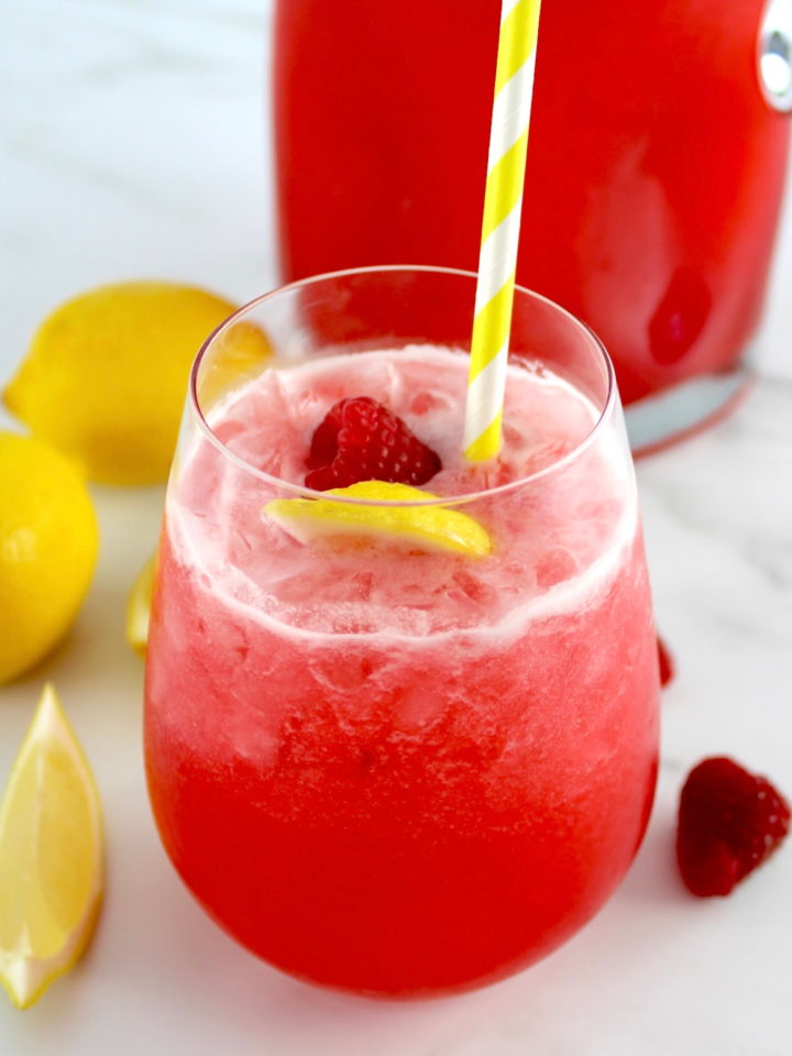 Raspberry Lemonade in glass with raspberry and lemon side with yellow straw