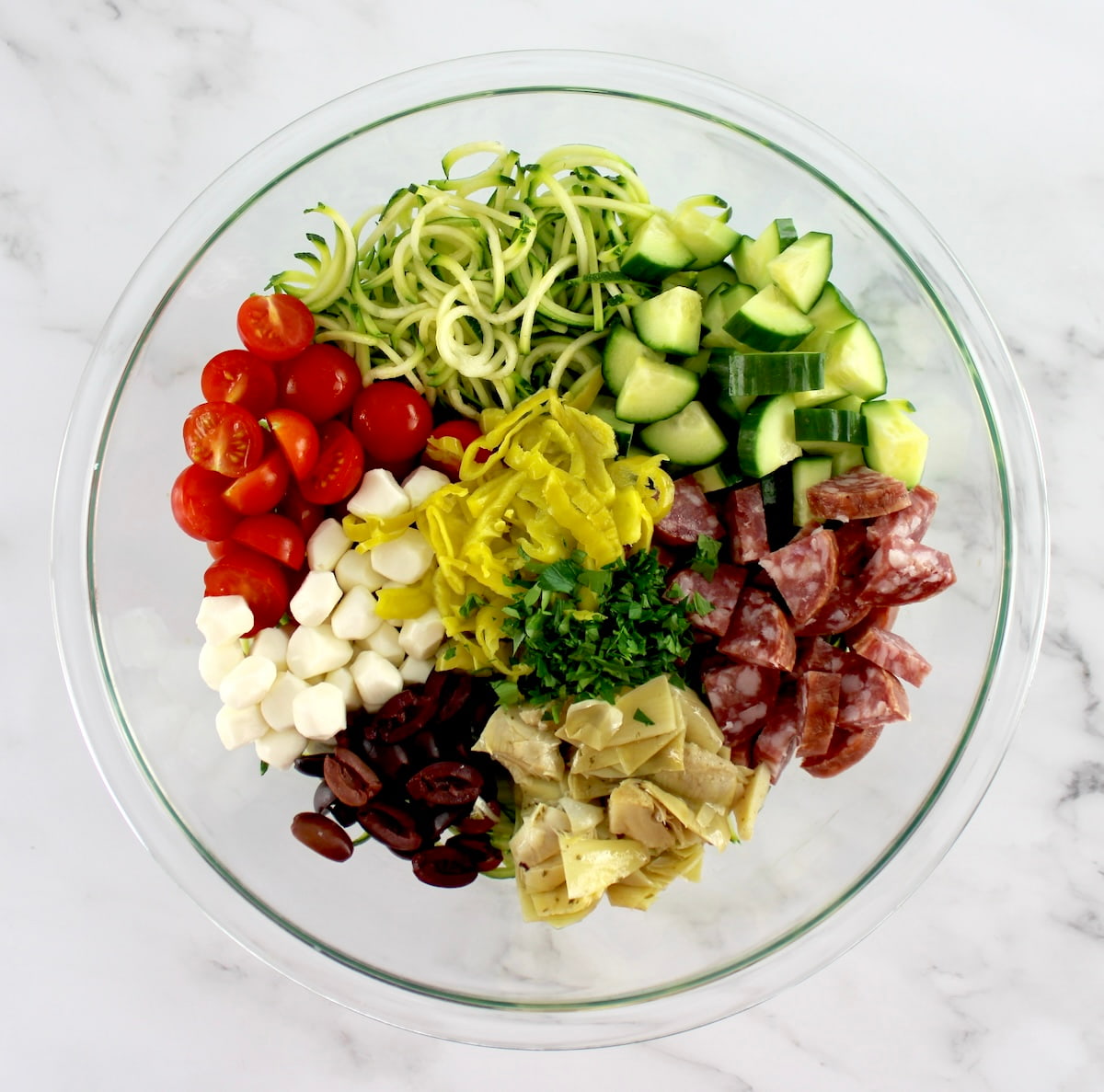 Zucchini Noodle Pasta Salad ingredients in glass bowl in sections unmixed