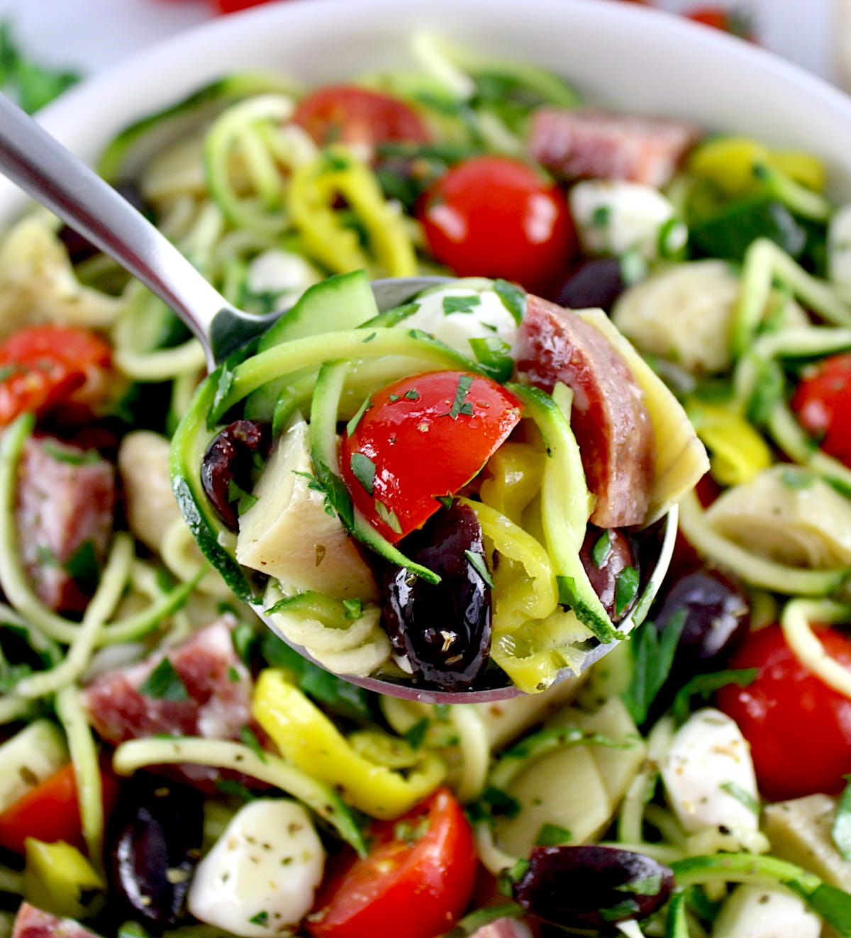 closeup of Zucchini Noodle Pasta Salad in silver spoon held up over bowl