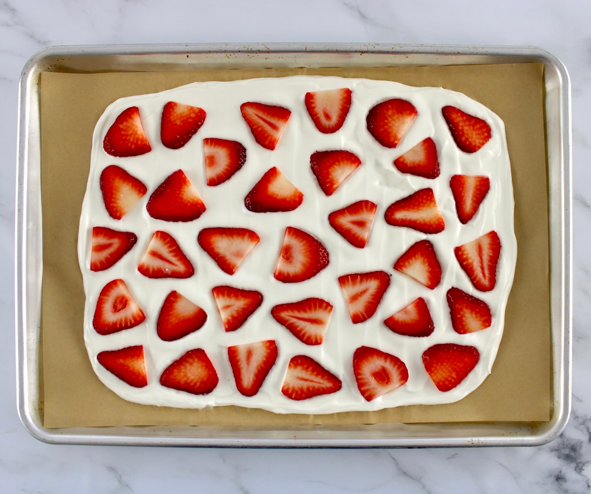 yogurt spread out on baking sheet with parchment with sliced strawberries on top