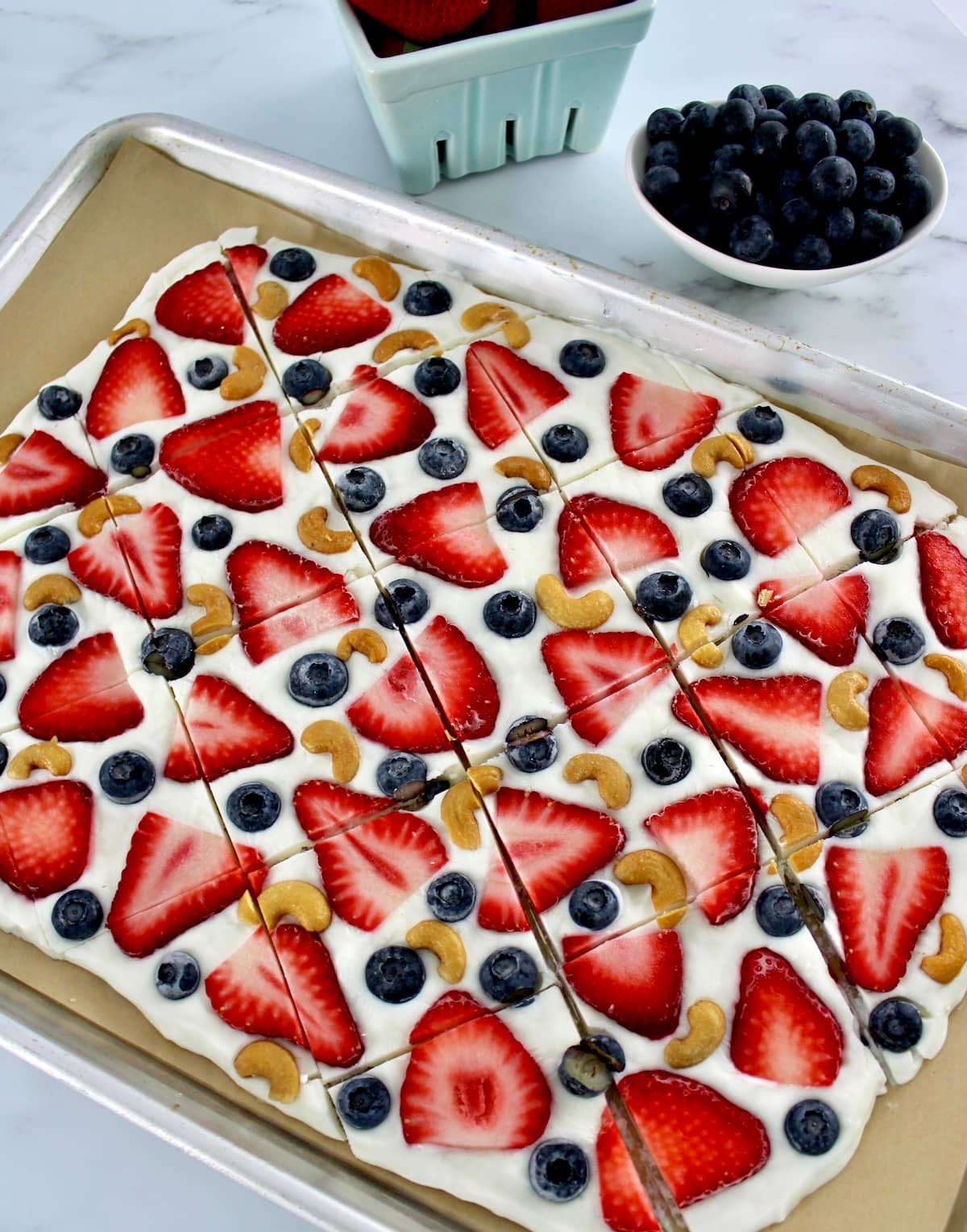 Frozen Yogurt Berry Bark on parchment lined baking sheet with berries in back