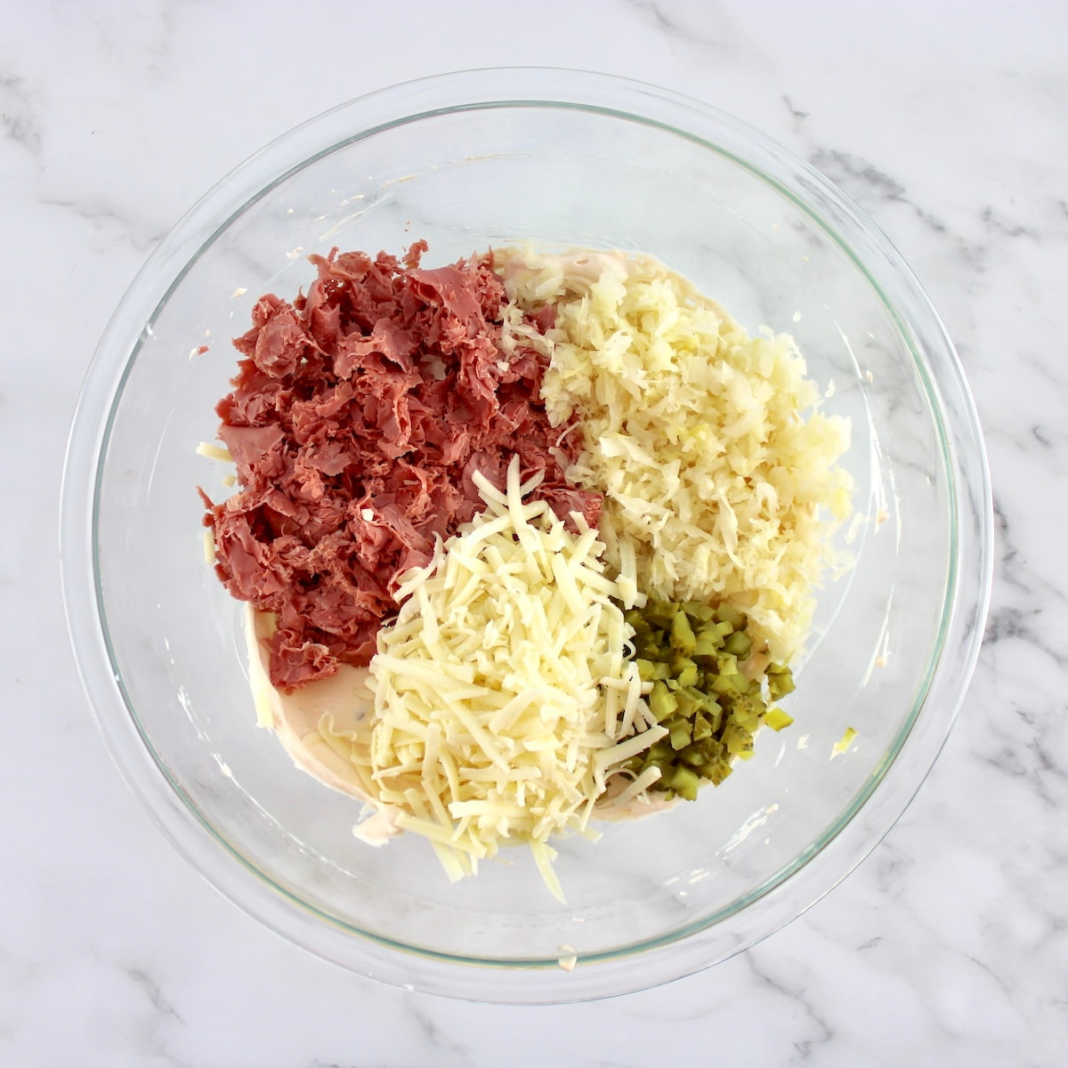 Hot Reuben Dip ingredients in glass bowl in sections unmixed