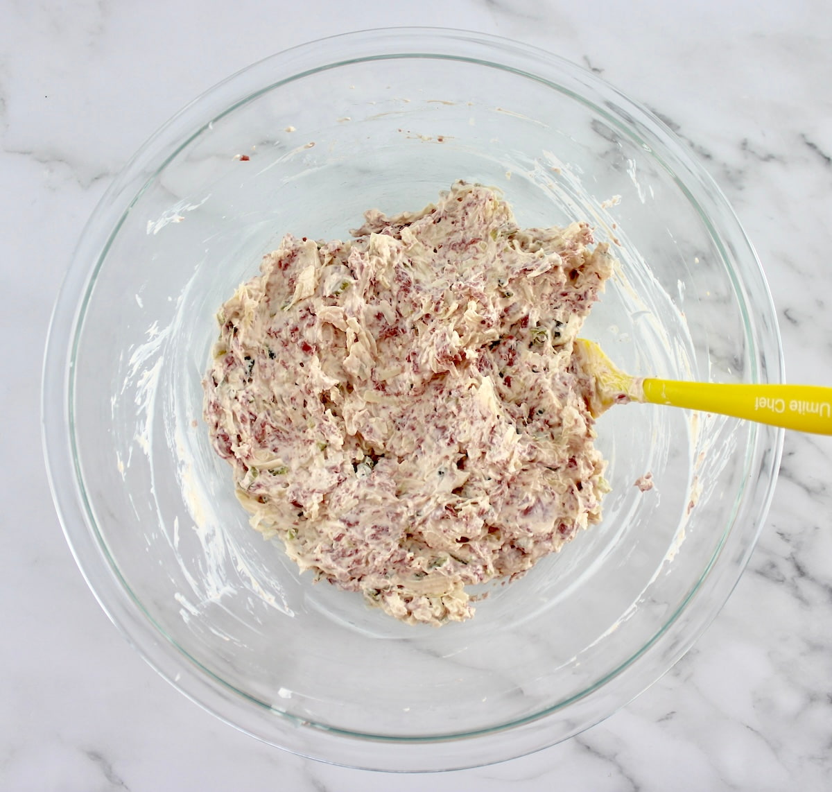 Hot Reuben Dip ingredients in glass bowl with yellow spoon