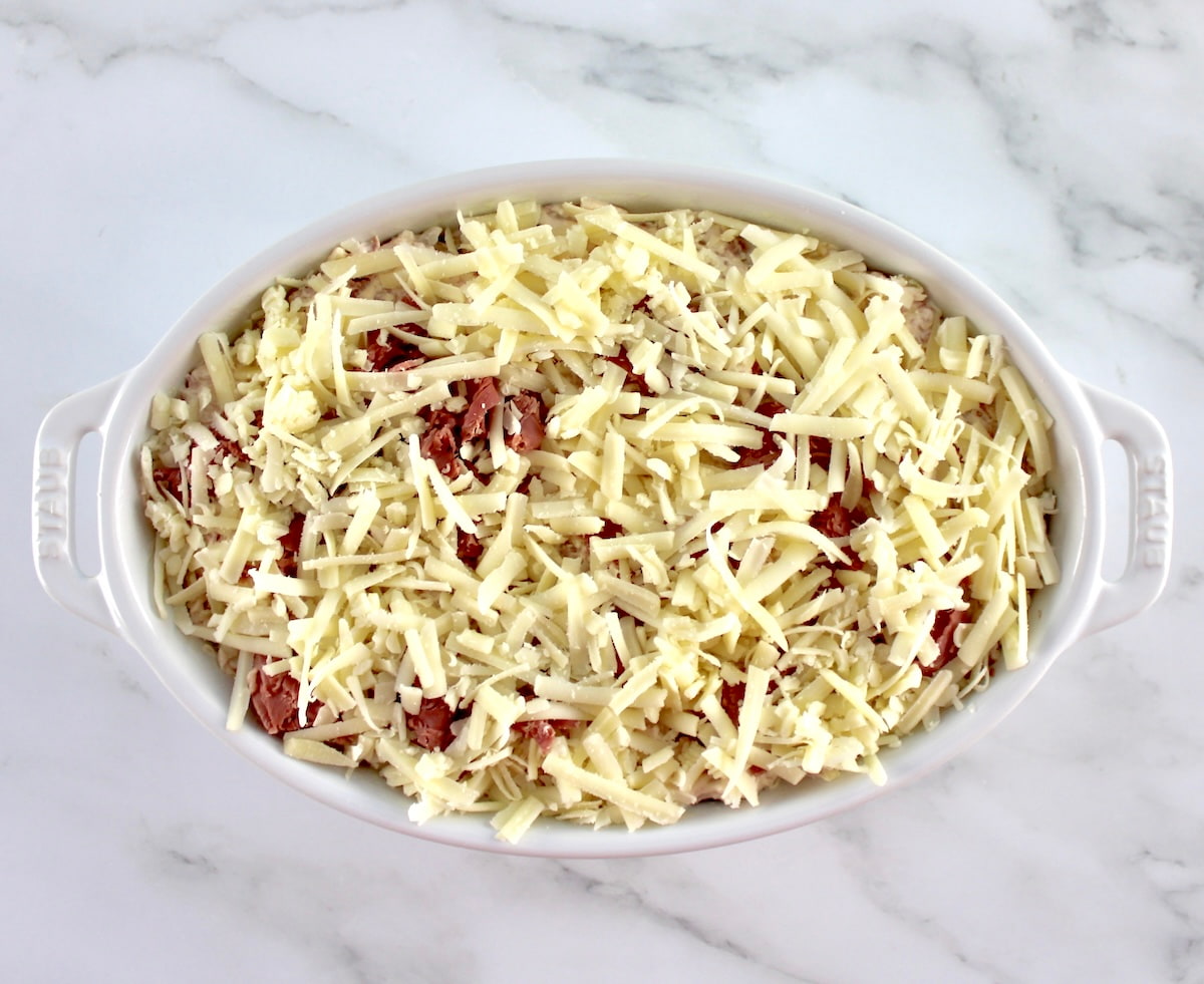 Hot Reuben Dip with shredded cheese on top in white oval casserole unbaked