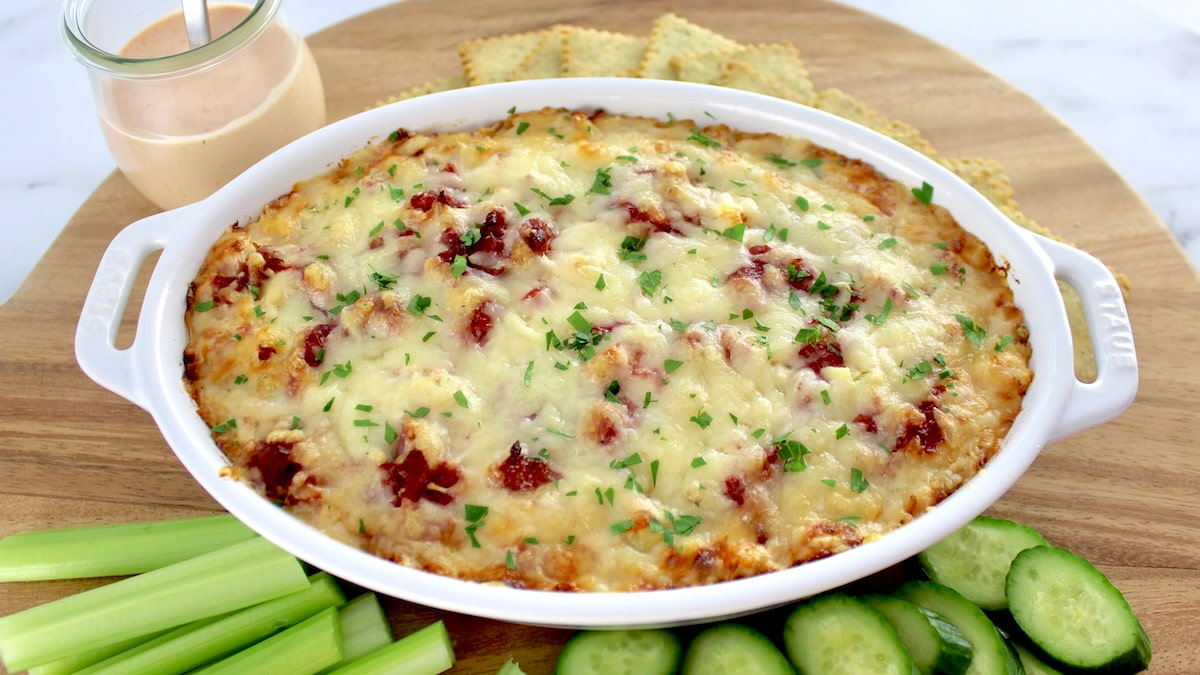 Hot Reuben Dip in oval casserole with crackers and veggies on side