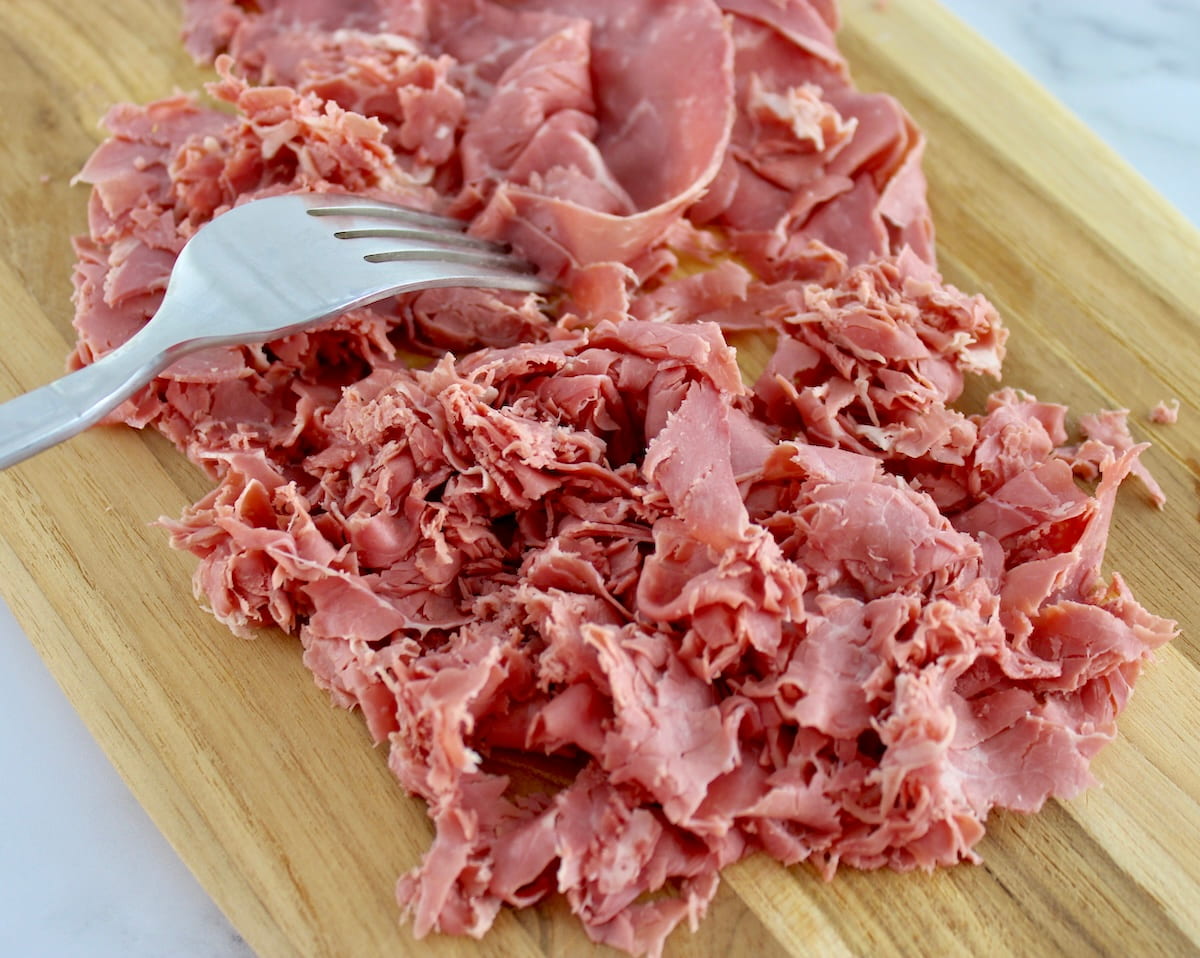 shredding corned beef on cutting board with fork