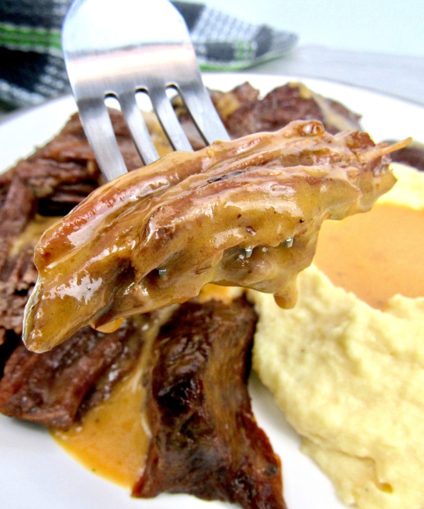 Instant Pot Roast piece on end of fork dripping gravy with mashed cauliflower in back