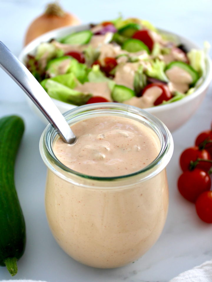 Keto Russian Dressing in open glass jar with spoon and salad in back