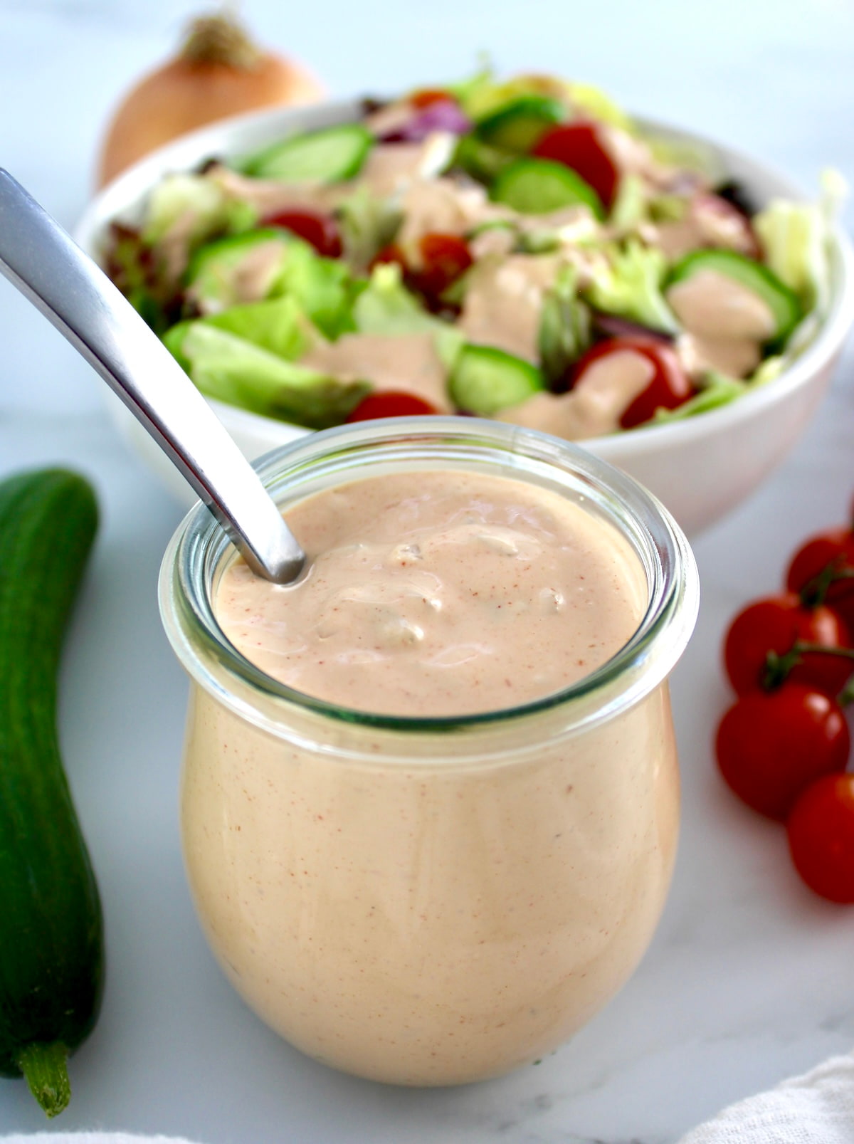 Keto Russian Dressing in open glass jar with spoon and salad in back