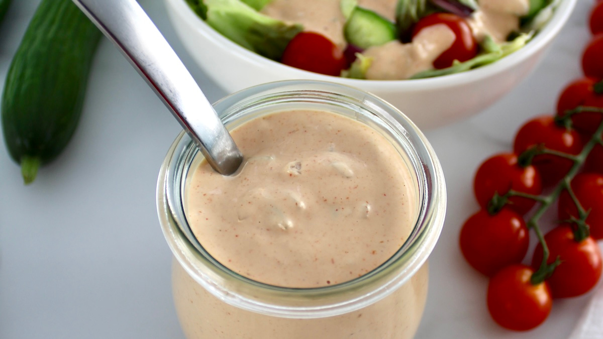 Keto Russian Dressing in open glass jar with spoon and salad in back