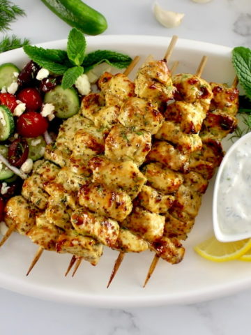 Air-Fryer-Greek-Chicken-Souvlak on white platter with Greek salad and dipping sauce