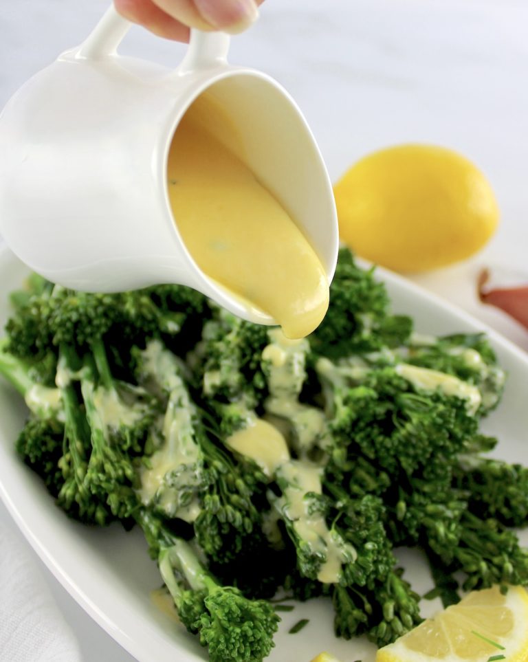 beurre blanc sauce being poured over broccoli on white plate