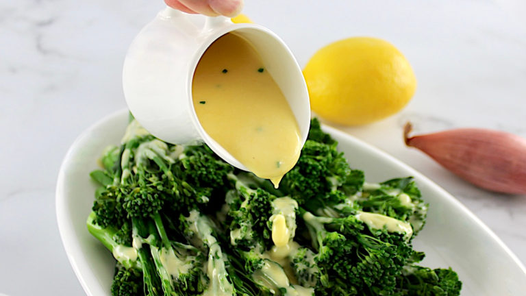 beurre blanc sauce being poured over broccoli on white plate