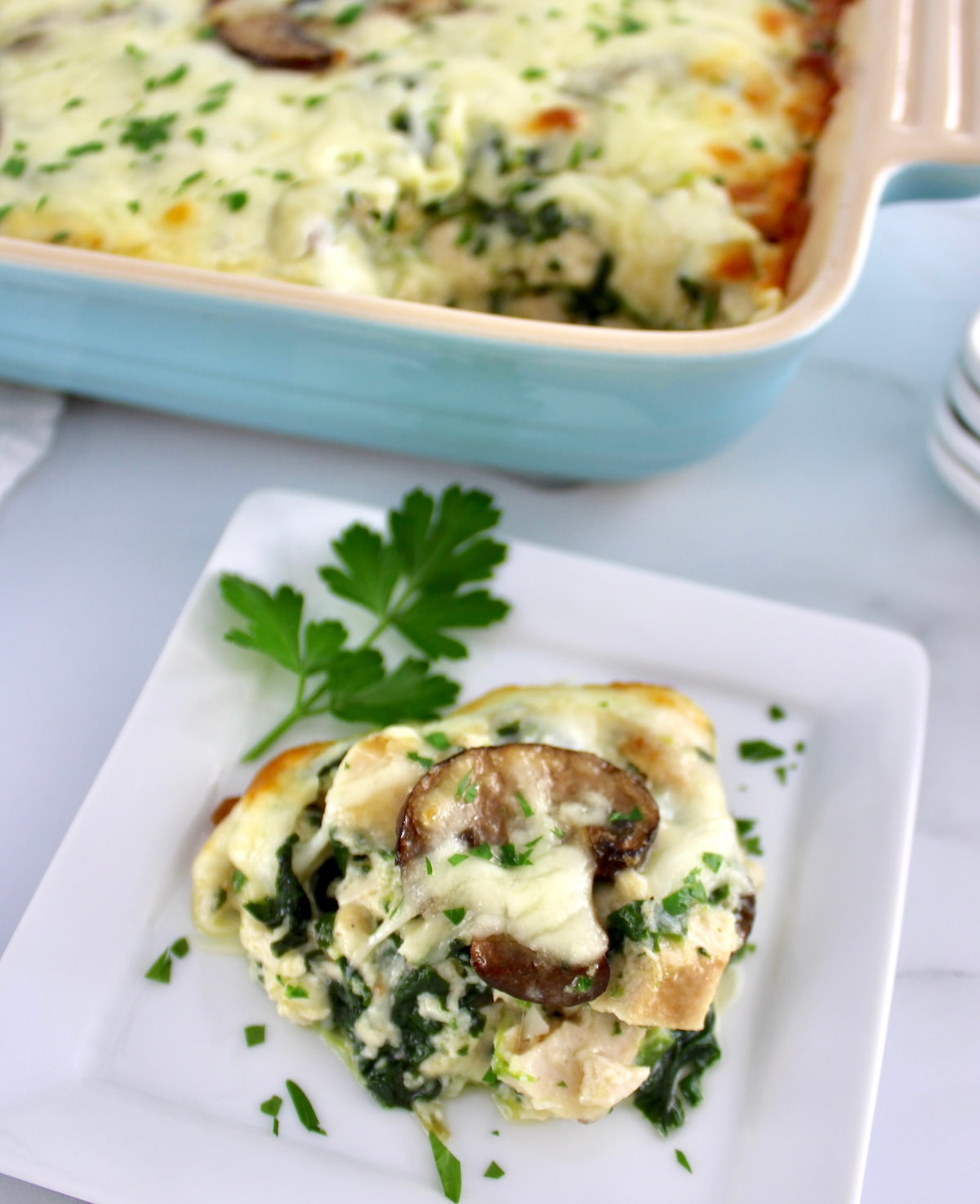 Chicken Alfredo Casserole serving on white square dish with casserole dish in background