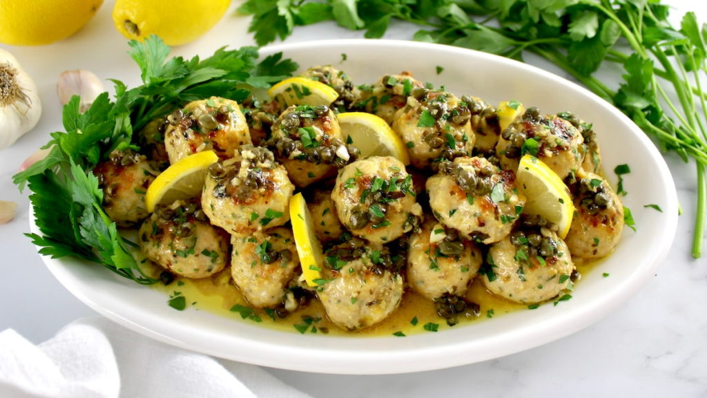 Chicken-Piccata-Meatballs on white oval platter with parsley and lemon slices garnish