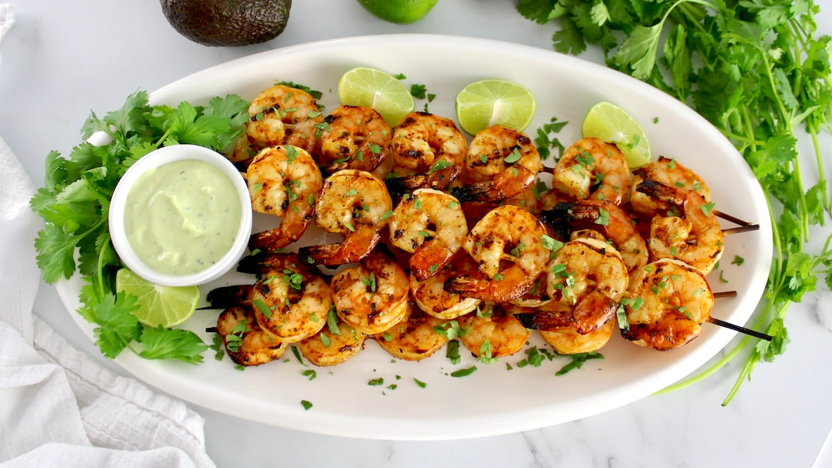 Grilled Lime Cilantro Shrimp Skewers on white oval platter with avocado ranch, lime and cilantro on side