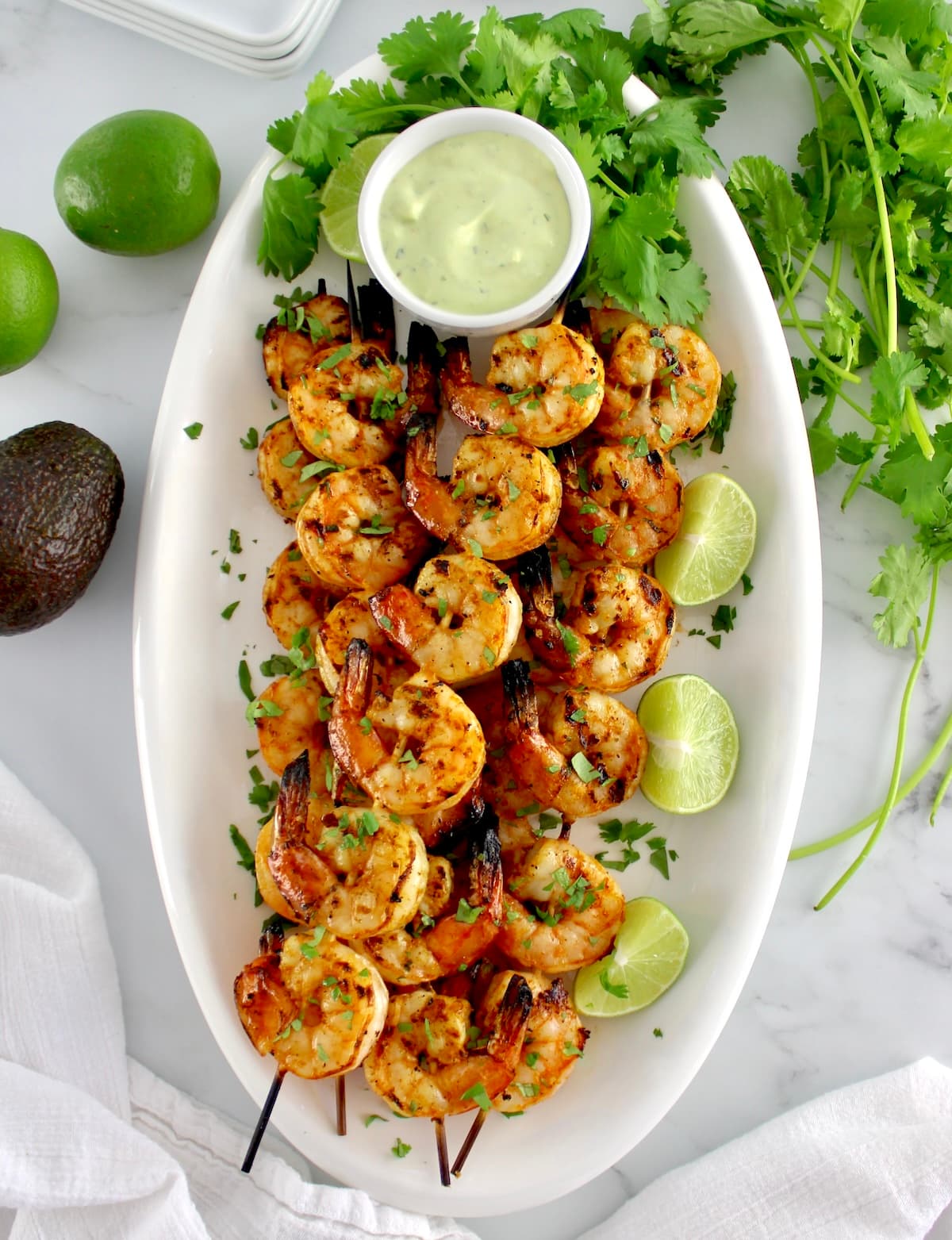 overhead view of Grilled Lime Cilantro Shrimp Skewers on white oval platter with avocado ranch sauce on side
