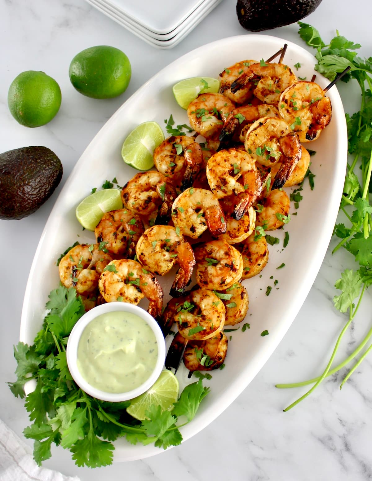 Grilled Lime Cilantro Shrimp Skewers on white oval platter with avocado ranch sauce on side