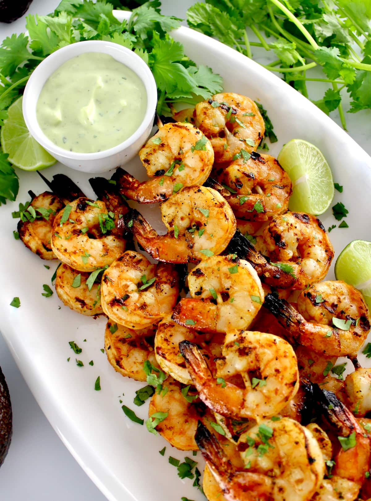 Grilled Lime Cilantro Shrimp Skewers on white platter with avocado ranch, cilantro and lime on side
