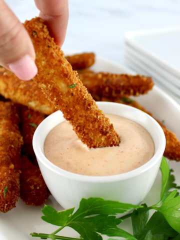 holding Halloumi Fry dipping into zesty dipping sauce in white bowl